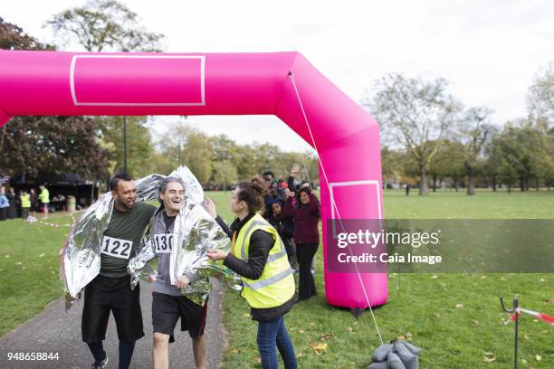 volunteer wrapping male runners in thermal blanket at marathon finish line - marathon runner finish line stock pictures, royalty-free photos & images