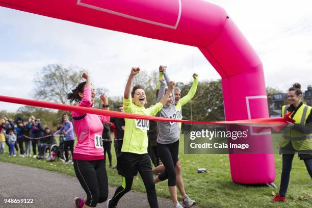 enthusiastic family runners crossing charity run finish line in park - finish line ribbon stock pictures, royalty-free photos & images