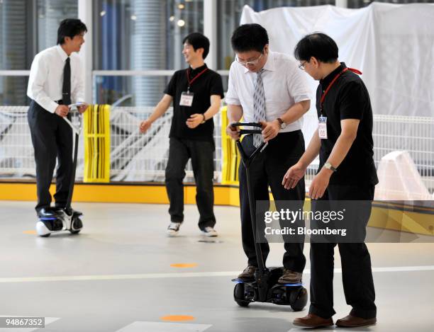 Journalists try to ride on Toyota Motor Corp.'s newly developed personal transport assistance robot "Winglet" type L in Tokyo, Japan, on Friday, Aug....