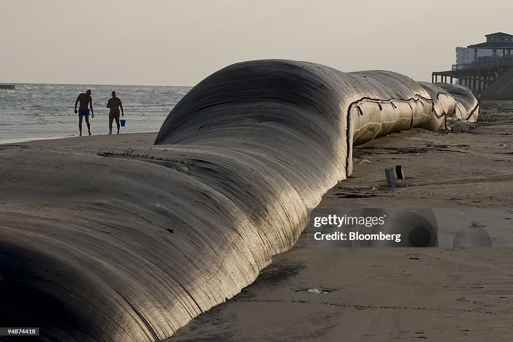 Beach goers walk alongside an artificial sandwall exposed du