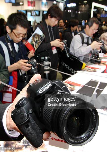 Visitors look at Canon Inc.'s EOS digital cameras displayed at the Photo Imaging Expo 2008 in Tokyo, Japan, on Wednesday, March 19, 2008. Canon Inc....