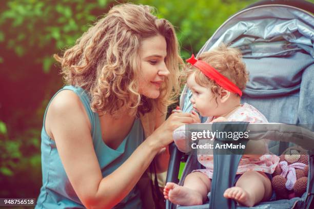 mother and her baby daughter in stroller in park - carrinho de criança imagens e fotografias de stock