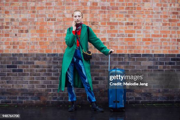 Model Sasha Komorova talks on the phone and wears a green coat, red printed scarf, a red shirt, blue multi-color patch jeans, black boots, a black...