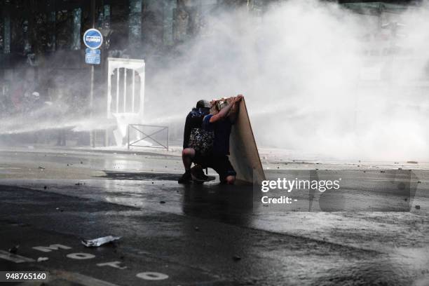 Protesters protect themselves with a piece of plywood as anti-riot police officers use a water cannon to disperse protesters during clashes on the...