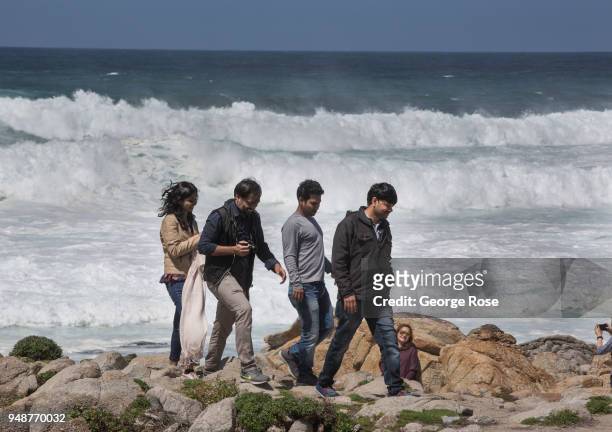 People take pictures while large ocean waves crash on the shoreline rocks near Spanish Bay, located along the famed 17-Mile Drive, on April 10 in...