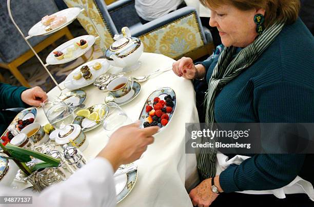 Waiter serves a plate of berries to Patti McGuire during tea service in the Palm Court at the Plaza Hotel in New York, U.S., on Monday, March 17,...