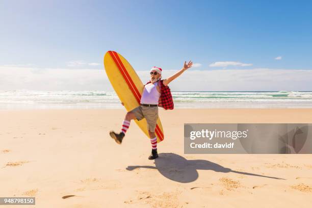 australische weihnachtsmann mit einem surfbrett am strand im sommer - beach christmas stock-fotos und bilder
