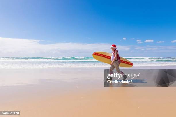 australian santa with a surfboard at the beach in summer - surfing santa stock pictures, royalty-free photos & images
