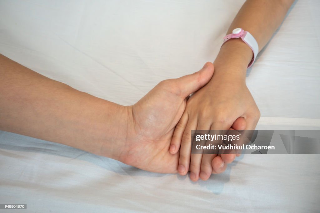 Parent holds the hand of a sick child in a hospital. Mother hand care about her kid.