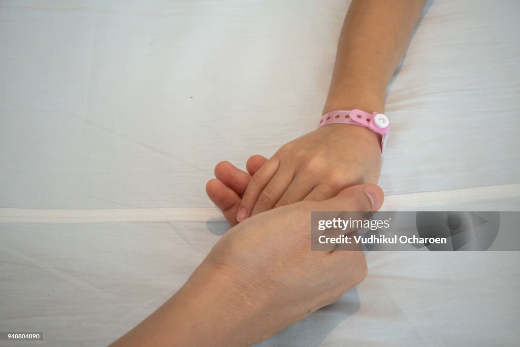 Parent holds the hand of a sick child in a hospital. Mother hand care about her kid.