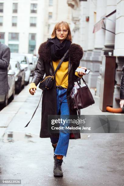 English model Fran Summers holds an iPhone and wears a brown leather coat with a fur collar, a black scarf, yellow sweater, blue jeans, a black...