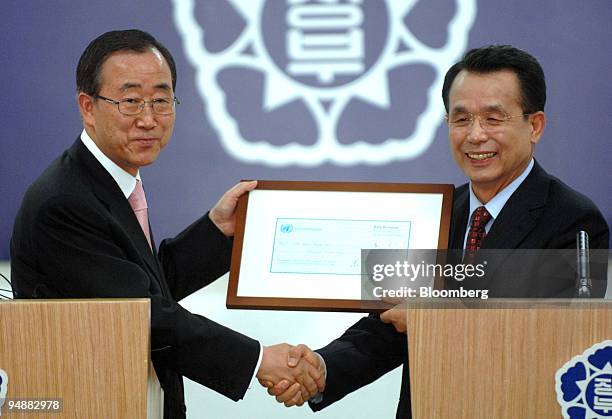 Ban Ki Moon, United Nations secretary-general, left, gives an one-dollar paycheck to Han Seung Soo, South Korea's prime minister, during their joint...