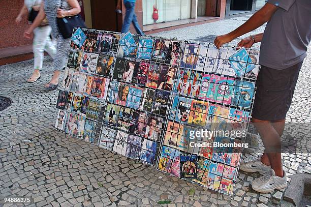 Pedestrians walks past a person selling pirated DVDs on the sidewalk of Rio Branco Avenue in downtown Rio de Janeiro, Monday, November 14, 2005. In...
