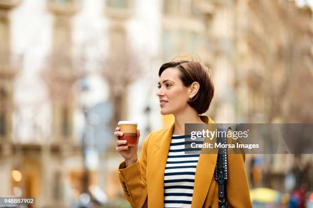 mid adult woman holding disposable cup in city - plastic cup stock pictures, royalty-free photos & images