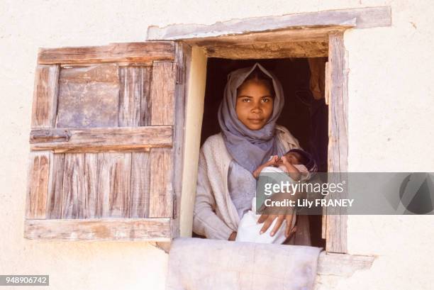 Jeune maman avec son bébé à sa fenêtre à Ambatondrazaka, en 1988, Madagascar.