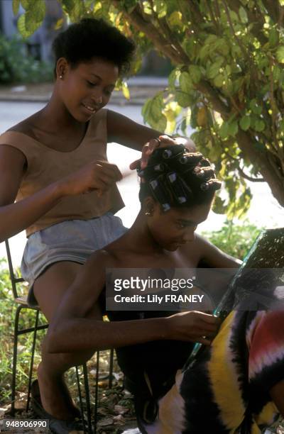 Jeune femme se faisant coiffer en extérieur dans un parc, la coiffeuse pose des bigoudis, en juillet 1991, à La Havane, Cuba.
