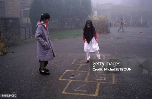 Petites filles musulmanes jouant à la marelle dans la cour d'une école publique de Batley, en 1989, Royaume-Uni.