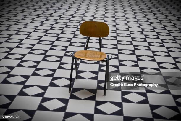 a wooden empty chair in the middle of an empty room with a decorated checkerboard floor - chess board without photos et images de collection