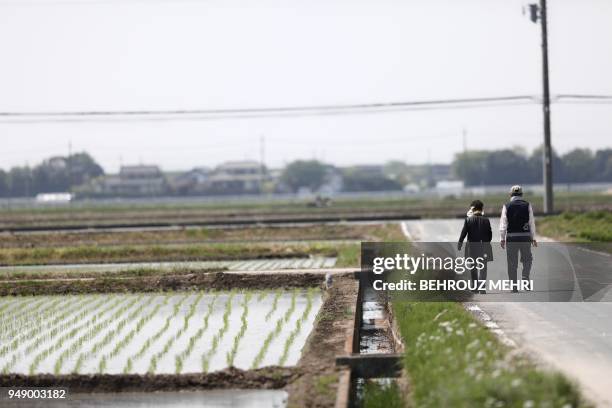 People walk past a rice paddy in Kazo city, Saitama prefecture on April 20, 2018.