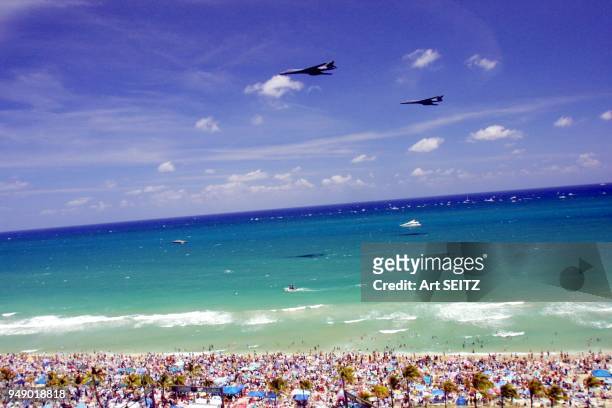 A pair ofus air force b-1-B lancer heavy bombers flying past colorful crowded beach during air and sea show.
