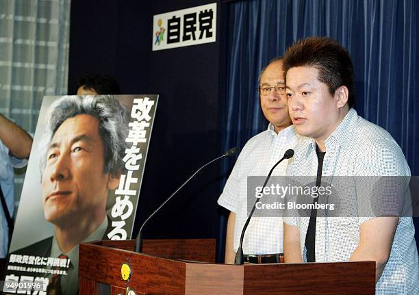 Livedoor President Takafumi Horie, right, speaks to reporters next to a poster of Japanese Prime Minister Junichiro Koizumi while Liberal Democratic...