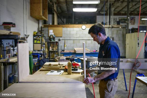 Worker glues pieces of wood together while making a kitchen cabinet at the Old Wood Co. Sustainable furniture manufacturing facility in Asheville,...