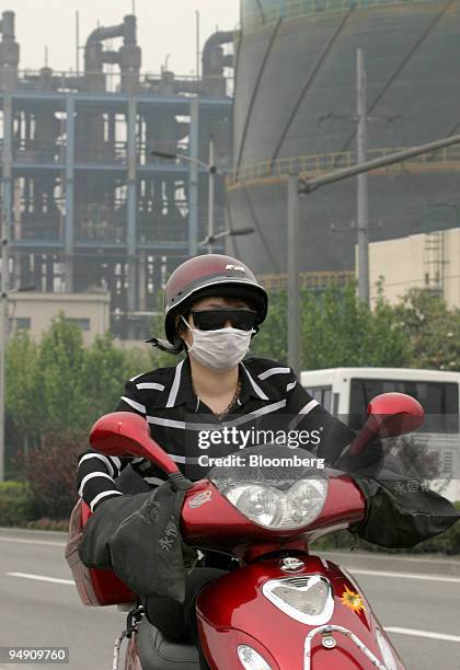 Woman wears a mask to filter out air pollution as she rides her motorcycle past the Shanghai Coking and Chemical Plant in Shanghai, China May 18,...