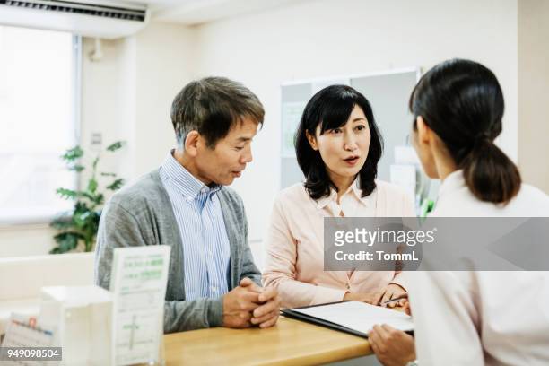 couple talking to nurse and filling out forms at hospital - asian receptionist stock pictures, royalty-free photos & images