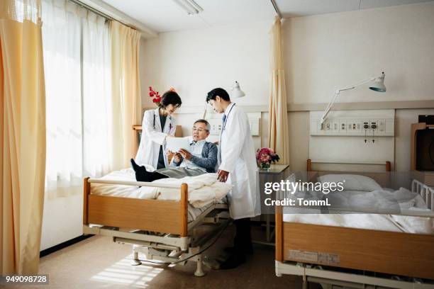 doctors tending to elderly patient in hospital bed - bedside manner stock pictures, royalty-free photos & images