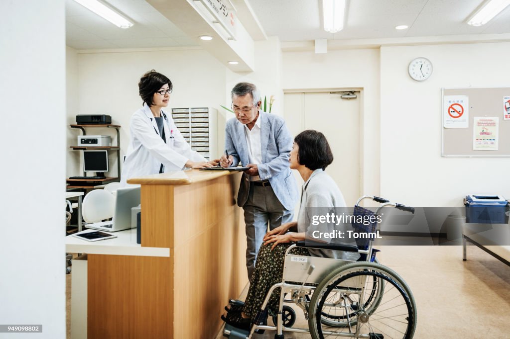 Nurse Helping Elderly Couple At Hospital Counter