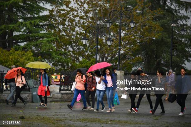 Girls walking with umbrellas during the wind storm and rain at Ridge on April 20, 2018 in Shimla, India. Shimla and surrounding areas witnessed a...