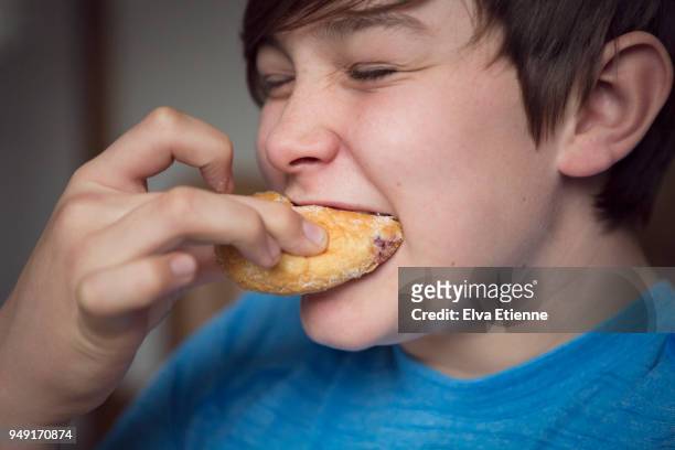 teenage boy biting into a sugary doughnut - teenager eating stock pictures, royalty-free photos & images