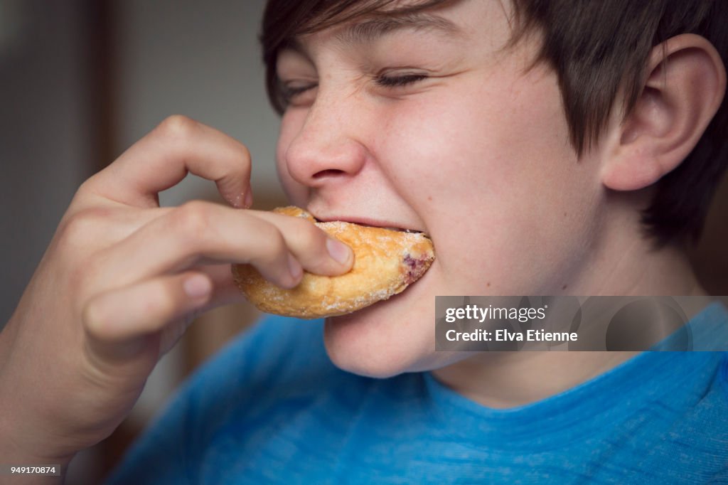 Teenage boy biting into a sugary doughnut