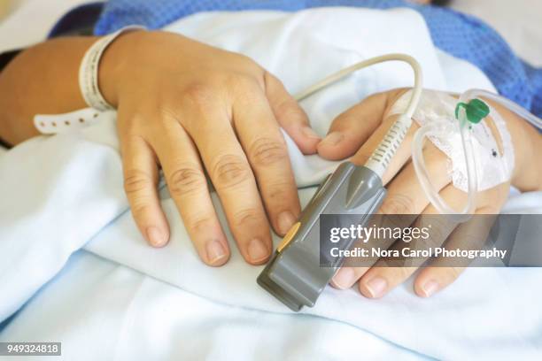 patient's hands with an iv drip and finger heart rate monitor - flebo salina foto e immagini stock