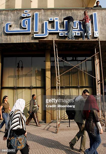 Pedestrians pass as workers make adjustments on an Egytrav travel agency sign in Cairo, Egypt, on Thursday, Nov. 27, 2008. Egypt's unemployment rate...