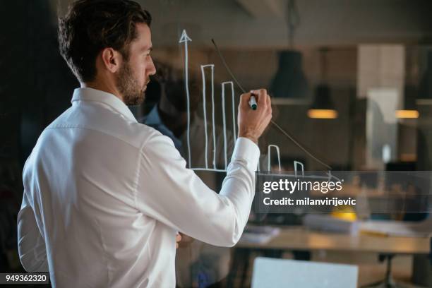 joven empresario gráfico de dibujo en la pared de cristal - director financiero fotografías e imágenes de stock