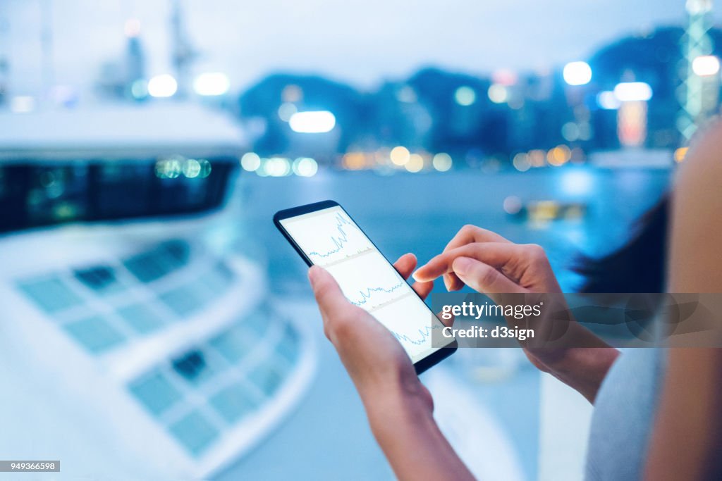 Woman checking stocks and shares data with smartphone in city