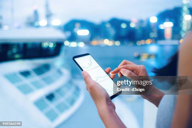 woman checking stocks and shares data with smartphone in city - market intelligence imagens e fotografias de stock