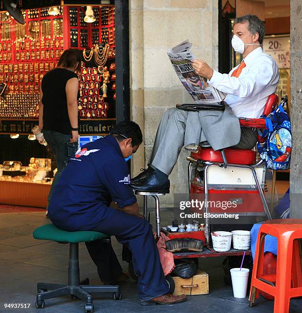 Man wearing a surgical mask reads a newspaper while getting his shoes shined in Mexico City, Mexico, on Monday, April 27, 2009. Mexican authorities...