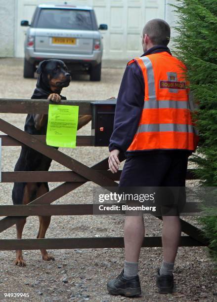 Postman Paul Haslegrave is greeted by a dog as he delivers letters on his rounds in Virginia Waters, Surrey, U.K., on Thursday, Feb. 26, 2009. The...
