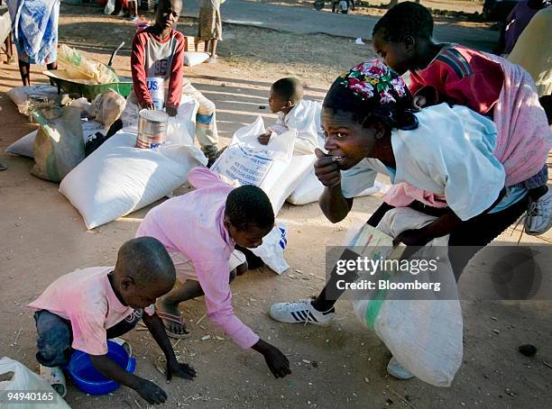 Mother and her children pick up maize kernels from the floor after being dropped at a food distribution point in Harare, Zimbabwe, on Thursday, April...