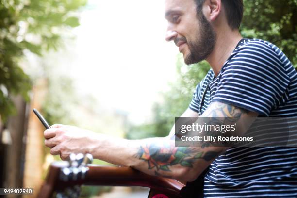 man using mobile phone while holding guitar - lilly roadstones stock pictures, royalty-free photos & images