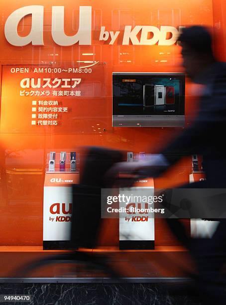 Man cycles past a display of KDDI Corp. Mobile phones outside an electronics store in Tokyo, Japan, on Thursday, April 23, 2009. KDDI Corp., Japan's...