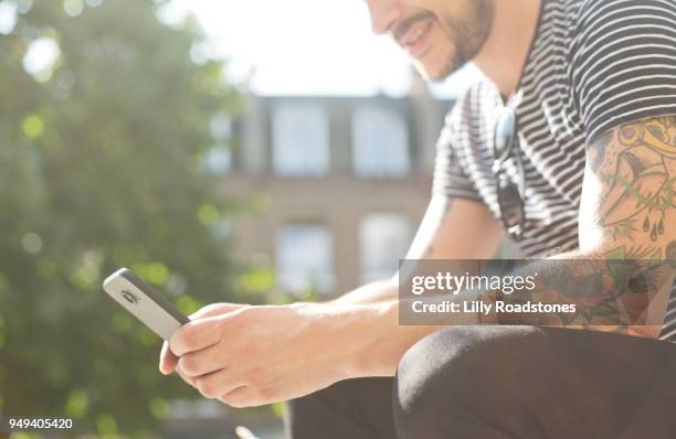 man with tattoos using mobile phone - lilly roadstones stock pictures, royalty-free photos & images