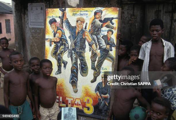 Enfants posant devant une affiche du film ?Delta Force 3? dessinée manuellement, à Elmina, Ghana.