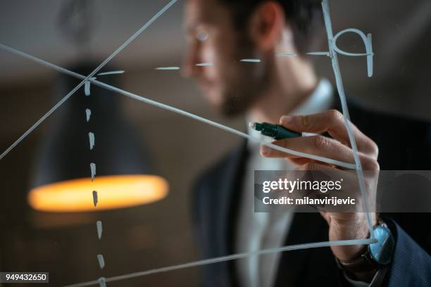 uomo che disegna il grafico della domanda di offerta sulla parete di vetro - cfo foto e immagini stock