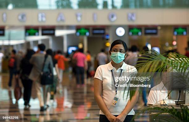 Health worker wearing a surgical mask watches as passengers walk by a thermal scanner upon arrival, at Changi airport in Singapore, on Monday, April...