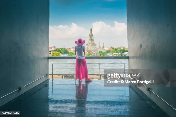 woman admiring the wat arun (temple of dawn) and chao phraya river, bangkok, thailand. - river chao phraya stock pictures, royalty-free photos & images