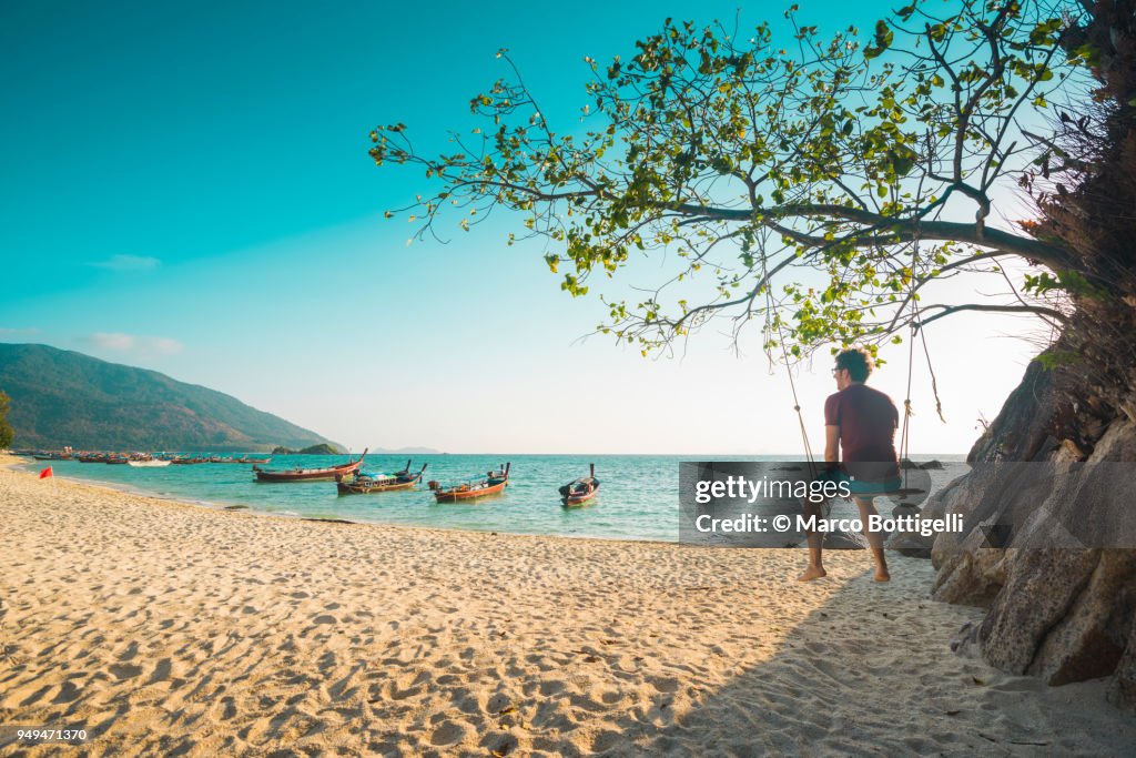 Tourist man sitting on swing at the beach, Thailand