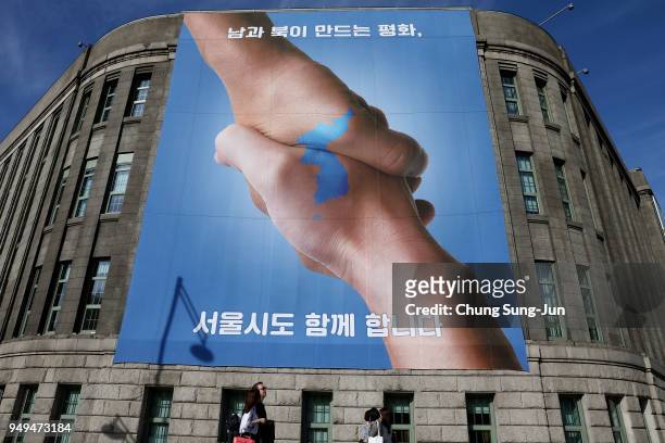Pedestrians walk by a banner showing a map of the Korean peninsular to wish for a successful inter-Korean summit on April 21, 2018 in Seoul, South...